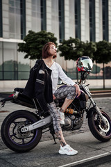 Super stylish looking girl is sitting on her purple motorcycle. She wears a black motorcycle jacket and plaid pants.