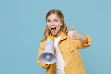 Excited little blonde kid girl 12-13 years old in yellow jacket posing isolated on pastel blue background. Childhood lifestyle concept. Mock up copy space. Screaming in megaphone showing thumb up.