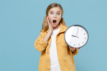 Shocked little blonde kid girl 12-13 years old in yellow jacket posing isolated on blue wall...