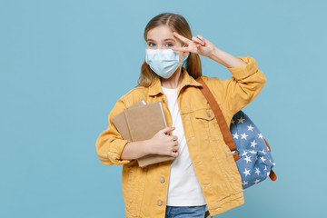 Little kid schoolgirl 12-13 years old in face mask backpack isolated on blue wall background....