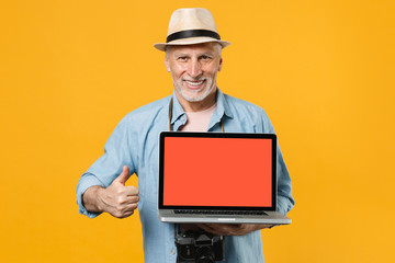 Smiling traveler tourist elderly gray-haired man isolated on yellow background. Passenger traveling on weekend. Air flight journey. Hold laptop with blank screen booking taxi hotel showing thumb up.