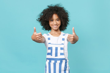 Smiling little african american kid girl 12-13 years old in casual striped clothes isolated on blue wall background studio portrait. Childhood lifestyle concept. Mock up copy space. Showing thumbs up.