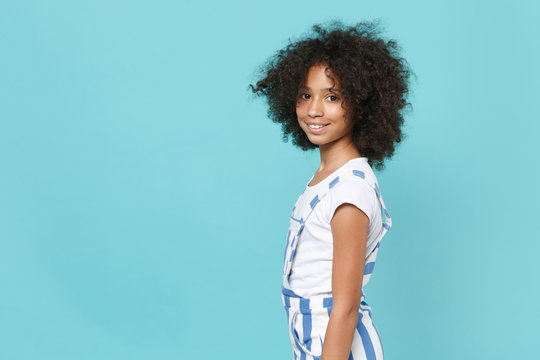 Side view of smiling little african american kid girl 12-13 years old in striped clothes isolated on blue background studio portrait. Childhood lifestyle concept. Mock up copy space. Looking camera.