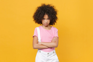 Obraz na płótnie Canvas Offended little african american kid girl 12-13 years old in pink t-shirt isolated on yellow background children studio portrait. Childhood lifestyle concept. Mock up copy space. Hold hands crossed.