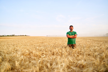 Happy farmer proudly standing in wheat field with arms crossed on chest. Agronomist wearing...