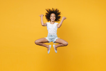 Full length portrait of cheerful little african american kid girl 12-13 years old in white t-shirt isolated on yellow wall background. Childhood lifestyle concept. Jumping, pointing thumbs aside.