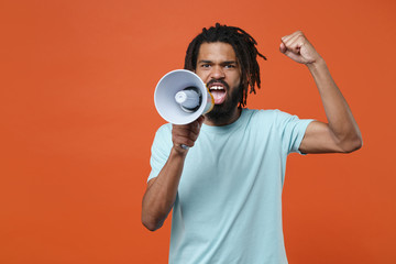 Displeased young african american man guy wearing blue casual t-shirt posing isolated on bright orange wall background studio portrait. People lifestyle concept. Screaming in megaphone clenching fist.