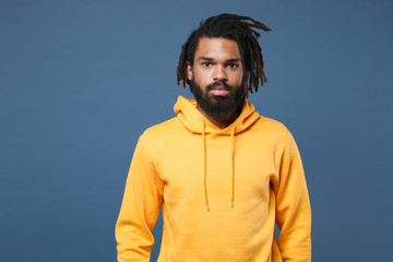 Young african american man guy wearing casual yellow streetwear hoodie posing isolated on blue wall...