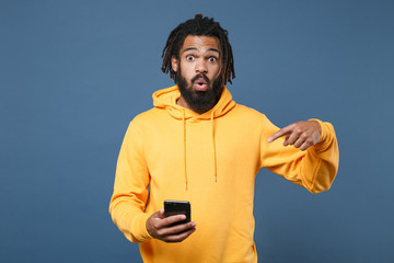 Shocked young african american man guy wearing yellow streetwear hoodie posing isolated on blue...