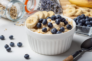 Oatmeal porridge with blueberries and banana on the table in a white Cup. Porridge with blueberries. Breakfast with oatmeal and banana.