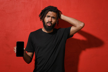 Worried young african american man 20s in black casual t-shirt posing hold mobile phone with blank...