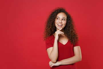 Pensive young african american woman girl in casual t-shirt posing isolated on red background studio portrait. People lifestyle concept. Mock up copy space. Put hand prop up on chin, looking aside.