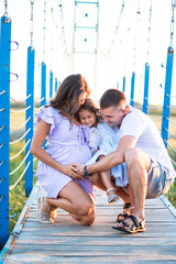 happy young family are hugging on the bridge in the sunset light. husband and a little girl touching pregnant wife's belly