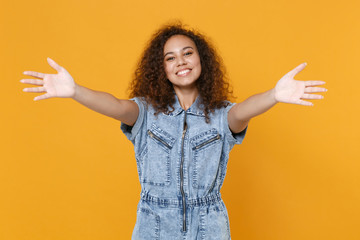 Smiling young african american woman girl in casual denim clothes isolated on yellow background studio portrait. People lifestyle concept. Mock up copy space. Stand with outstretched hands for hugs.