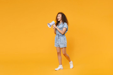 Full length portrait of cheerful young african american woman girl in denim clothes isolated on yellow wall background studio portrait. People lifestyle concept. Screaming on megaphone, looking aside.