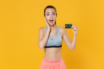 Shocked young fitness sporty woman in sportswear working out isolated on yellow background. Workout sport motivation lifestyle concept. Mock up copy space. Hold credit bank card, put hand on cheek.
