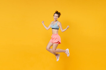 Fototapeta na wymiar Full length portrait overjoyed fitness woman in sportswear working out isolated on yellow background. Workout sport motivation lifestyle concept. Mock up copy space. Jumping, doing winner gesture.