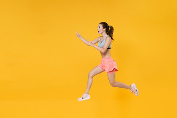 Fototapeta na wymiar Full length portrait excited fitness woman in sportswear working out isolated on yellow background. Workout sport motivation lifestyle concept. Mock up copy space. Jump, pointing index fingers aside.