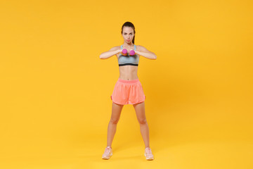 Fototapeta na wymiar Full length portrait of serious young fitness woman girl in sportswear working out isolated on yellow wall background studio. Workout sport motivation lifestyle concept. Doing exercise with dumbbell.