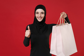 Smiling young arabian muslim woman in hijab black clothes posing isolated on red wall background....