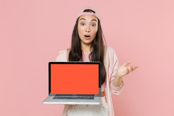 Naklejka premium Shocked young asian woman girl in casual clothes cap isolated on pastel pink background. People lifestyle concept. Mock up copy space. Hold laptop pc computer with blank empty screen spreading hands.