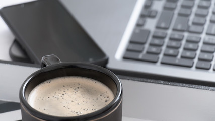 Primer plano de taza de café negra junto a una laptop y un teléfono móvil en una habitación...