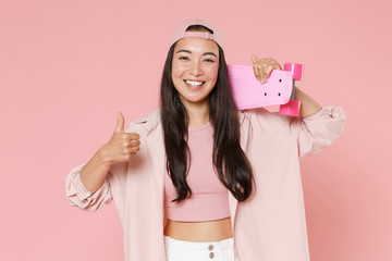 Smiling young asian woman girl in casual clothes, cap posing isolated on pastel pink wall background studio portrait. People lifestyle concept. Mock up copy space. Hold skateboard, showing thumb up.