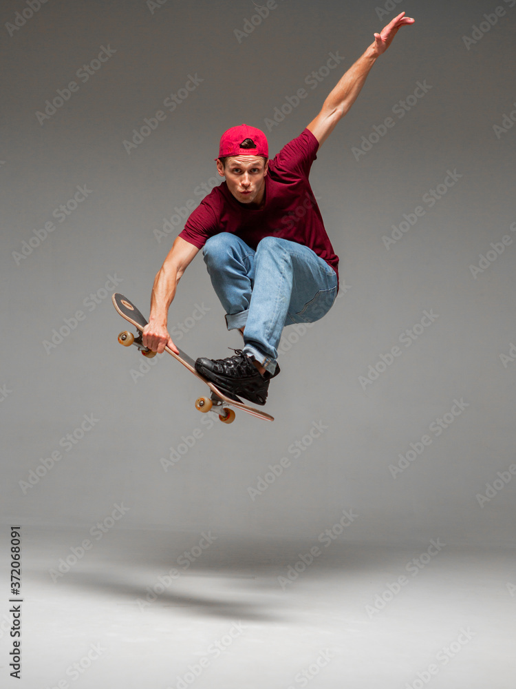 Wall mural cool young guy skateboarder jumps on skateboard in studio on gray background. photography about skat