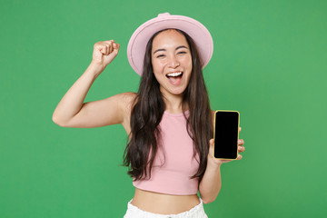 Happy young asian woman girl in casual pink clothes hat isolated on green background. People lifestyle concept. Mock up copy space. Hold mobile phone with blank empty screen, doing winner gesture.