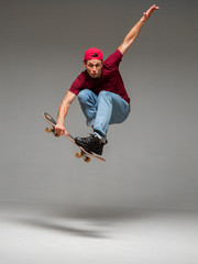 Cool young guy skateboarder jumps on skateboard in studio on gray background. Photography about skateboarding tricks