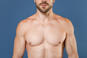 Fototapeta premium Cropped image of young bearded fitness sporty strong guy bare-chested muscular sportsman posing isolated on blue wall background studio portrait. Workout sport motivation lifestyle concept.