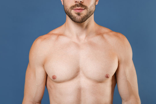 Cropped image of young bearded fitness sporty strong guy bare-chested muscular sportsman posing isolated on blue wall background studio portrait. Workout sport motivation lifestyle concept.