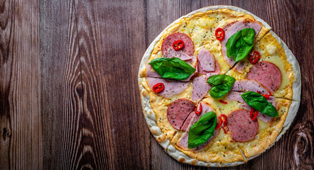 Pizza with Mozzarella cheese, ham, tomato sauce, salami, pepper, Spices and Fresh basil. Italian pizza on wooden table background