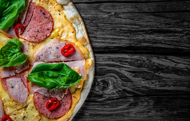 Pizza with Mozzarella cheese, ham, tomato sauce, salami, pepper, Spices and Fresh basil. Italian pizza on wooden table background