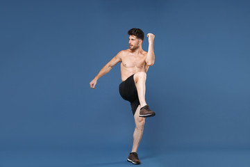 Obraz premium Full length portrait of young fitness sporty strong guy bare-chested muscular sportsman isolated on blue background. Workout sport motivation lifestyle concept. Doing stretching exercising for legs.