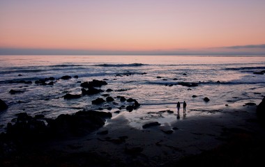 Obraz premium a young couple is dwarfed by the seascape as they look toward the sunset