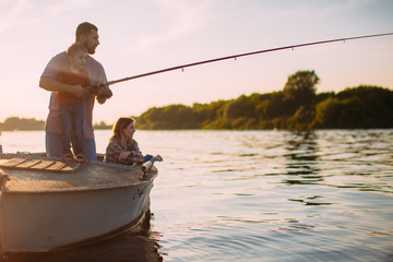 Young family fishing on boat on river in summertime. Father teaches son fishing. Photo for blog...