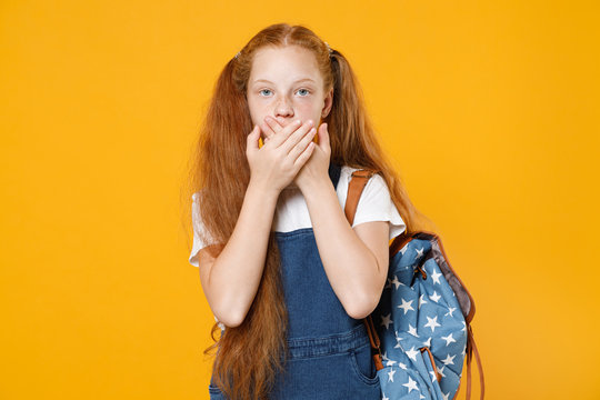 Young Confused School Teen Girl 12-13 In White T-shirt Blue Uniform Backpack Posing Cover Mouth Hands Isolated On Yellow Background Children Studio Portrait Childhood Kids Education Lifestyle Concept