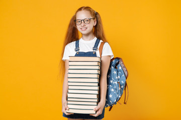 Young fun redhead girl 12-13 years old in white t-shirt eyeglasses backpack hold big stack school textbook notebook book isolated on yellow background children studio portrait Kids education concept - obrazy, fototapety, plakaty