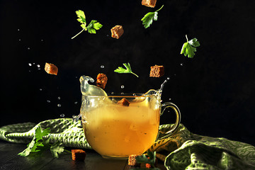 A cup of broth with flying ingredients and splashes on a dark background.