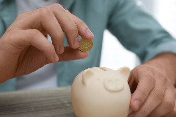 Man putting coin into piggy bank at wooden table, closeup
