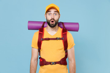 Shocked traveler young man in yellow casual t-shirt, cap with backpack isolated on blue background studio. Tourist traveling on weekend getaway. Tourism discovering hiking concept. Keeping mouth open.