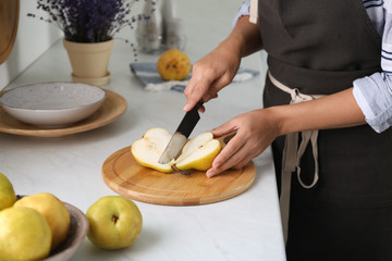 Woman cutting fresh ripe pear at table in kitchen, closeup