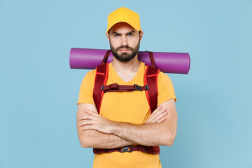 Displeased traveler young man in yellow casual t-shirt cap with backpack isolated on blue background. Tourist traveling on weekend getaway. Tourism discovering hiking concept. Holding hands crossed.