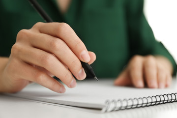 Woman drawing with pencil in notepad at white table, closeup