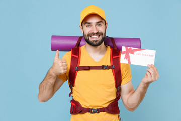 Smiling traveler young man in casual t-shirt cap backpack isolated on blue background. Tourist traveling on weekend getaway. Tourism discovering hiking concept. Hold gift certificate showing thumb up.