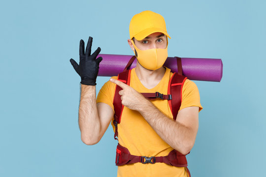 Traveler young man in face mask with backpack isolated on blue background. Tourist traveling on weekend getaway. Tourism discovering hiking concept. Pointing index finger on hand in sterile gloves.