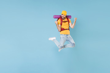 Fototapeta na wymiar Full length portrait Happy young traveler man in cap with backpack isolated on blue background. Tourist traveling on weekend getaway. Tourism discovering hiking concept. Jumping doing winner gesture.