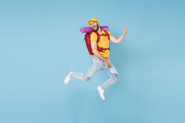 Naklejka na ściany i meble Full length portrait funny young traveler man in cap with backpack isolated on blue background. Tourist traveling on weekend getaway. Tourism discovering hiking concept. Jumping like playing guitar.