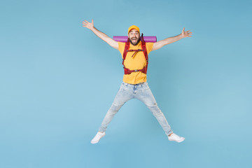 Full length portrait funny young traveler man in t-shirt cap backpack isolated on blue background. Tourist traveling on weekend getaway. Tourism discovering hiking concept. Jump spreading hands legs.